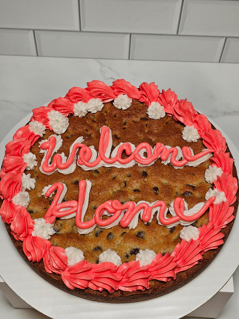 Large cookie cake with pink and white frosting on a white surface.